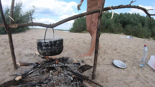 Naked girl cooks pasta on a bonfire